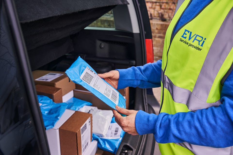 female courier holds takes small parcel from car boot filled with other parcels