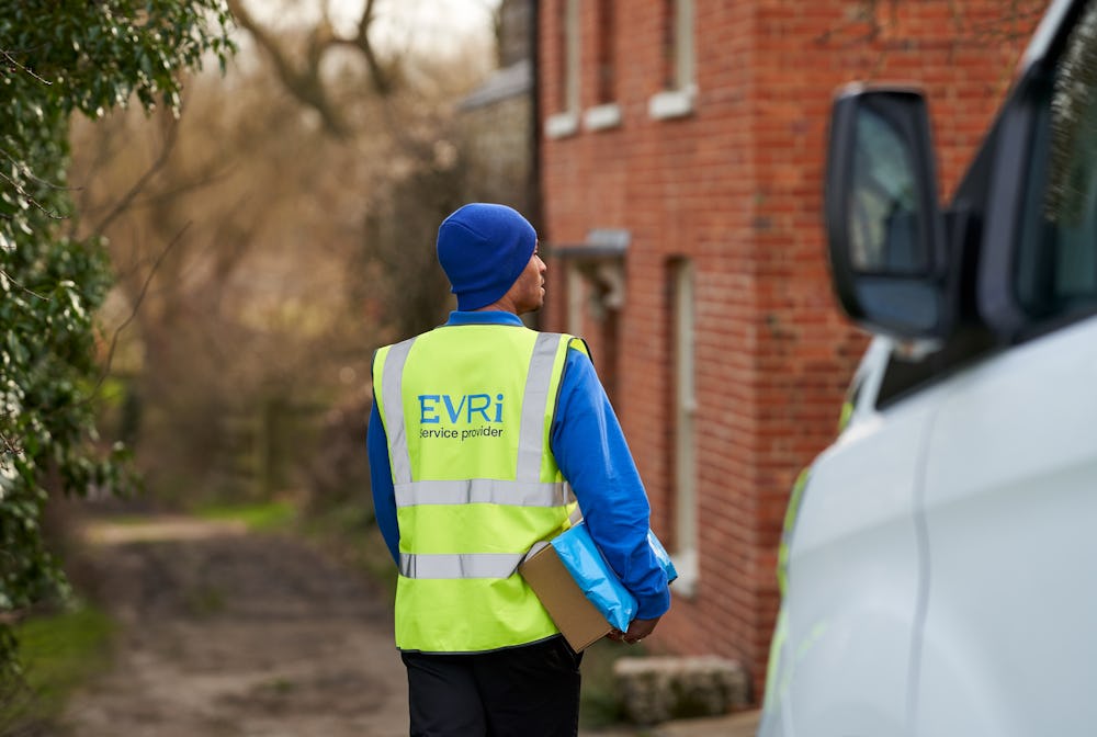 Photo of a courier outside of house by van holding parcels