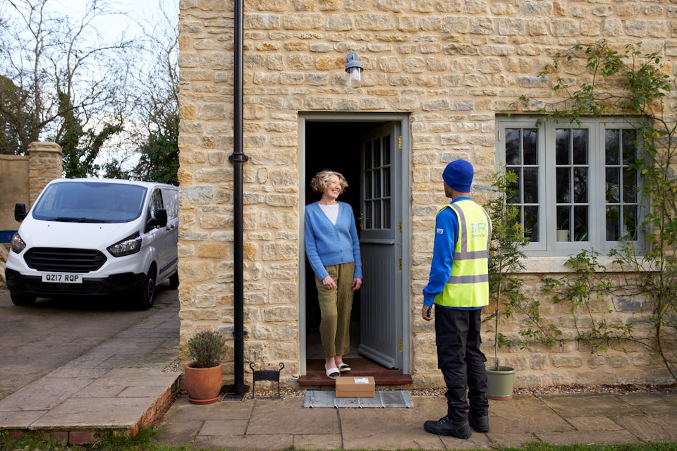 woman on cottage doorstep talking to courier in blue uniform