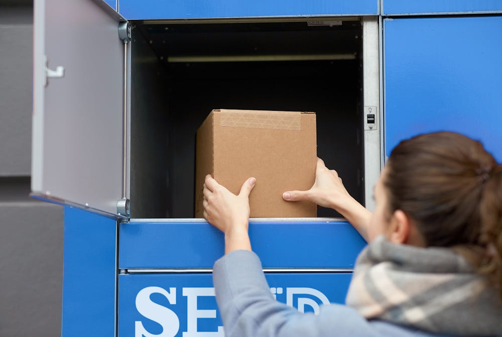 Woman opening blue locker to place cardboard box inside