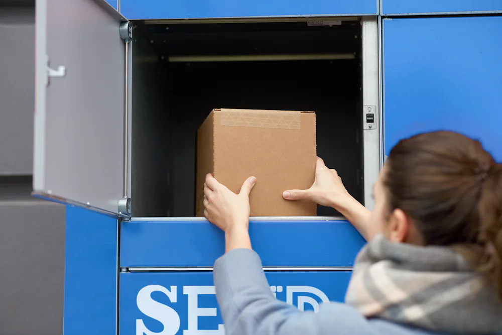 Woman opening blue locker to place cardboard box inside