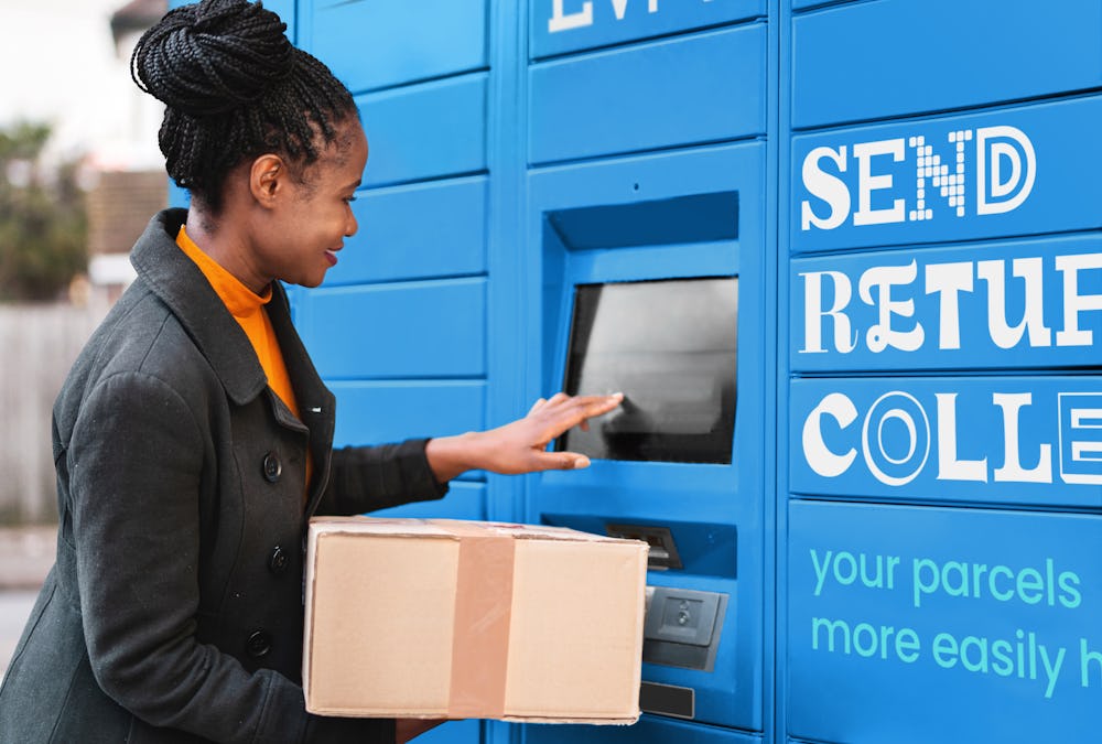 Woman using terminal on parcel locker while holding cardboard box