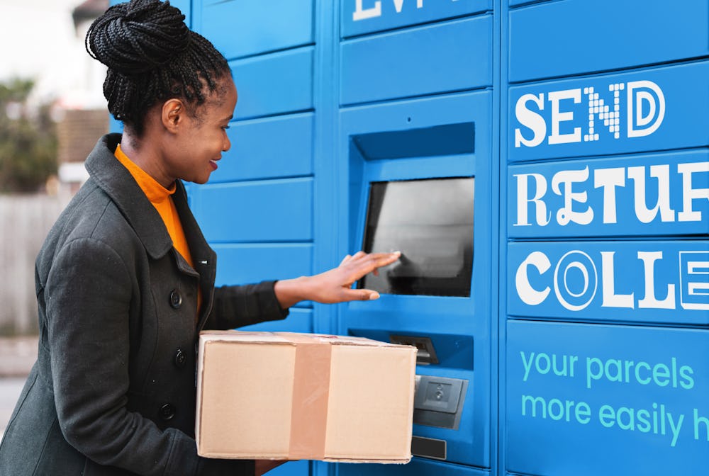 Woman using terminal on parcel locker while holding cardboard box