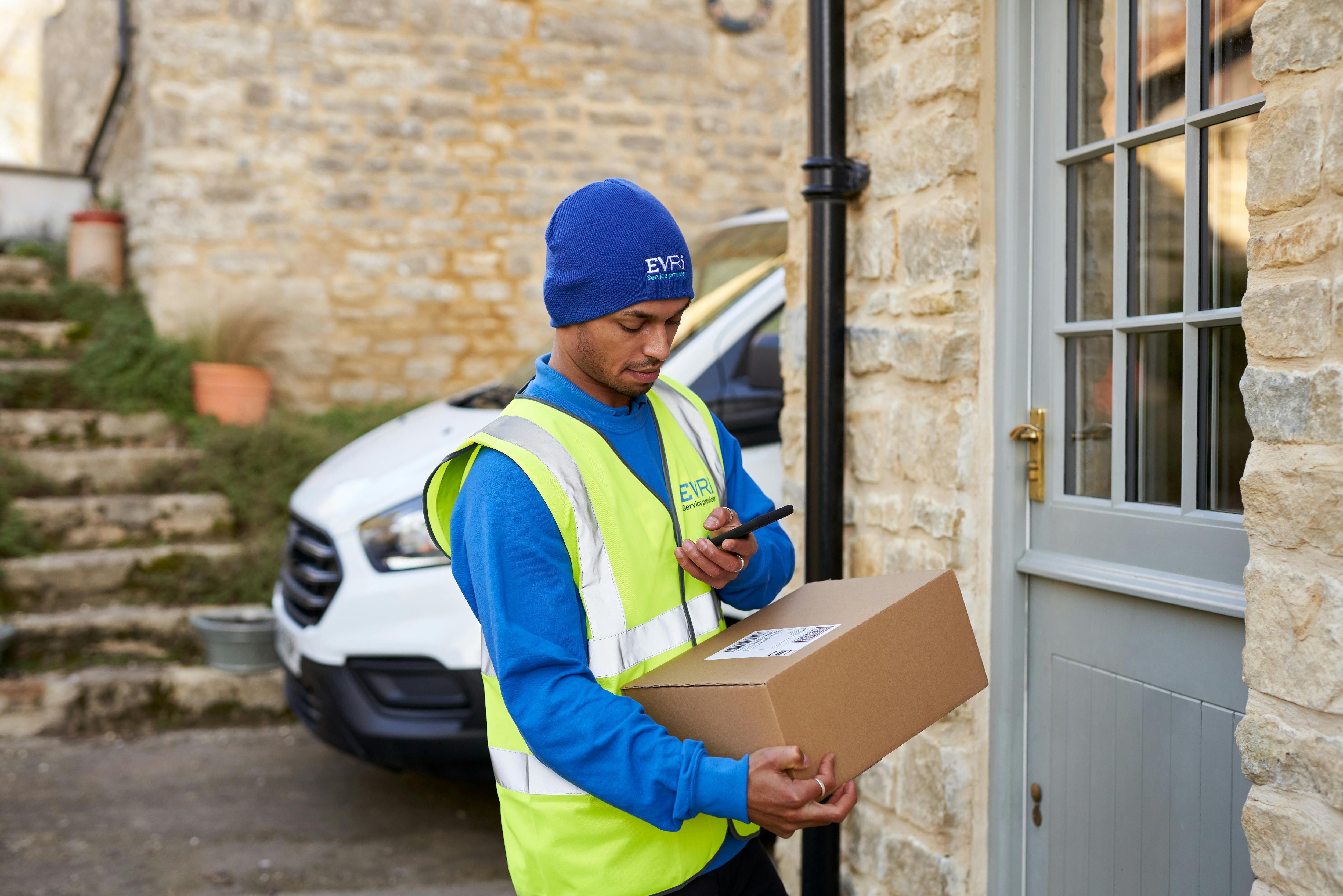 courier holding parcel on doorstep and scanning on smartphone
