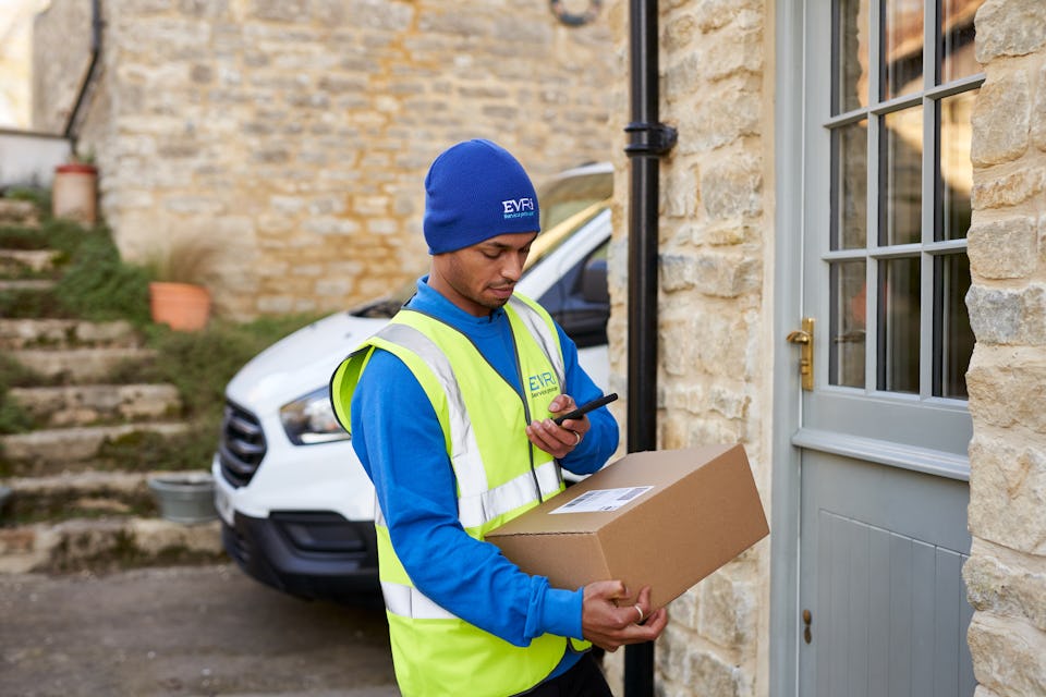 Photo of a courier holding parcel on doorstep and scanning on smartphone