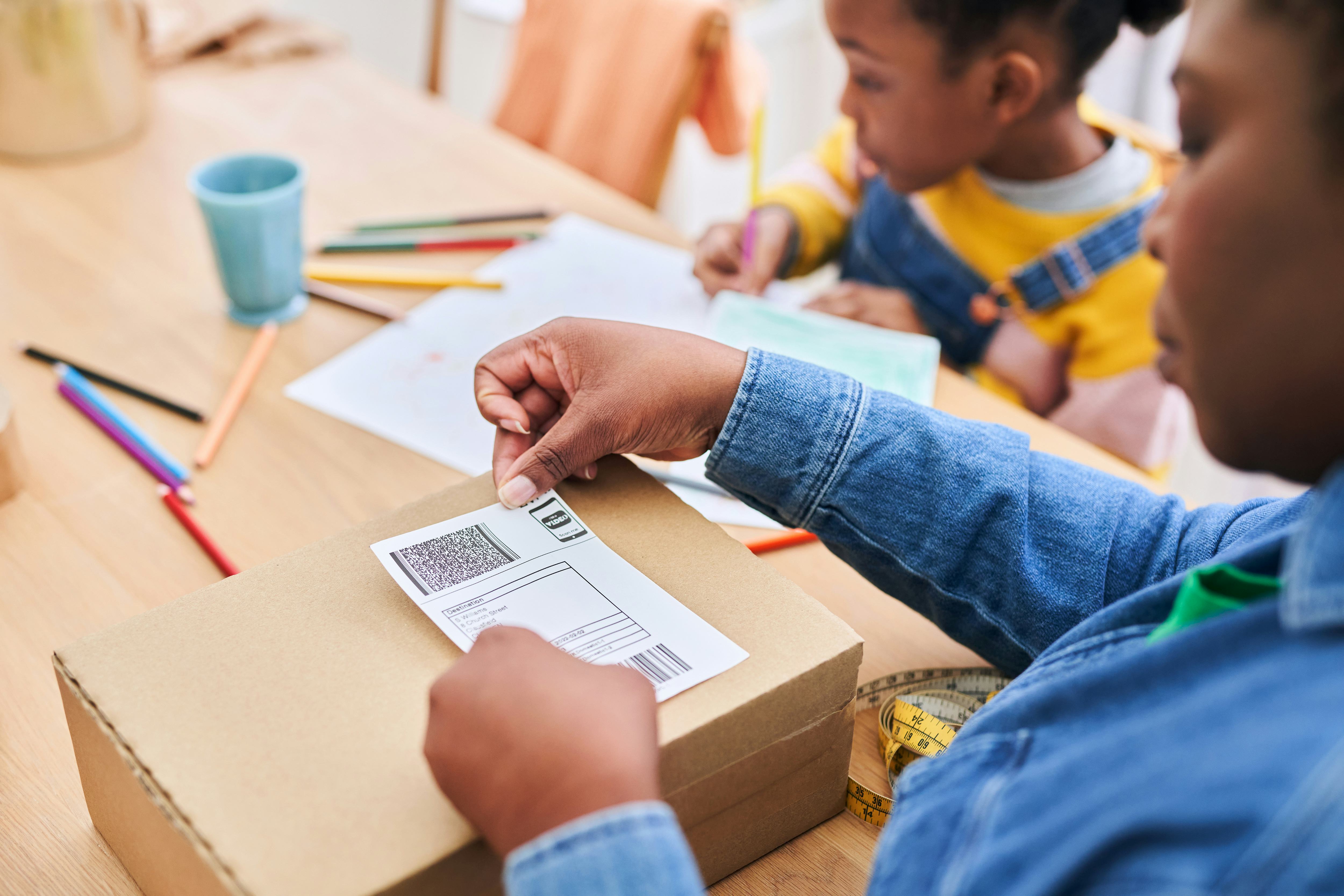 woman placing label on parcel while sat at table with child