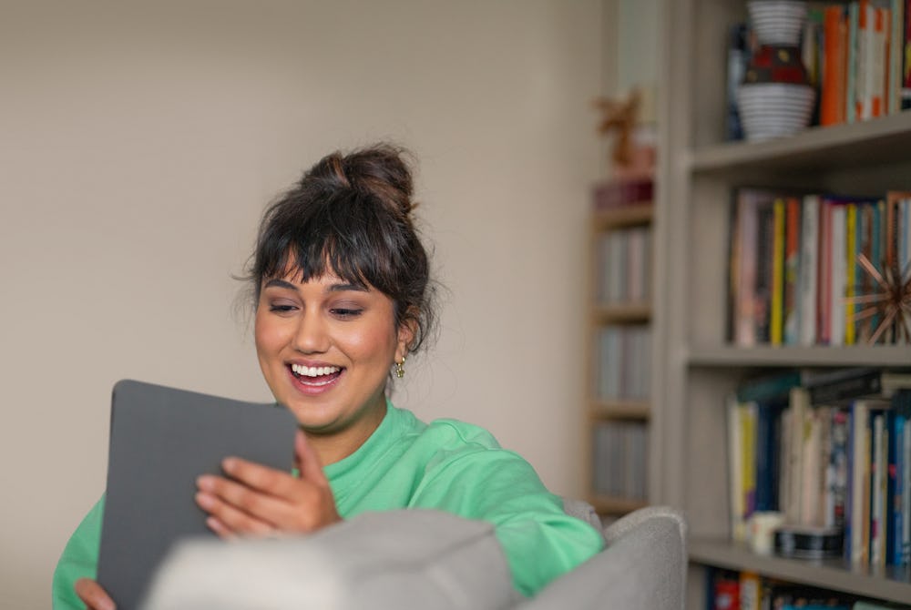 woman sat on sofa in living room holding tablet device and smiling