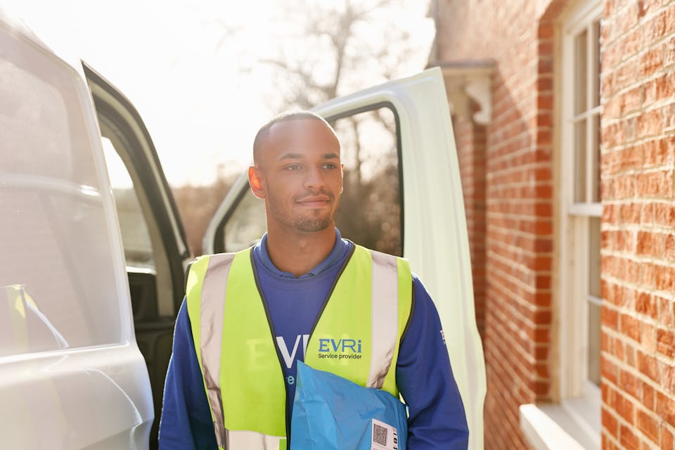 Photo of a courier next to white van approaching house with parcel