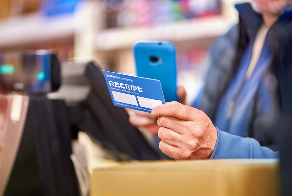 Cashier holding parcelshop receipt and smartphone