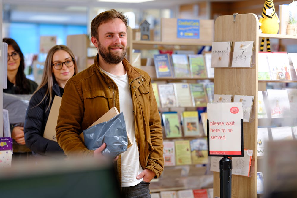 Man with parcel in the queue at a Post Office ParcelShop