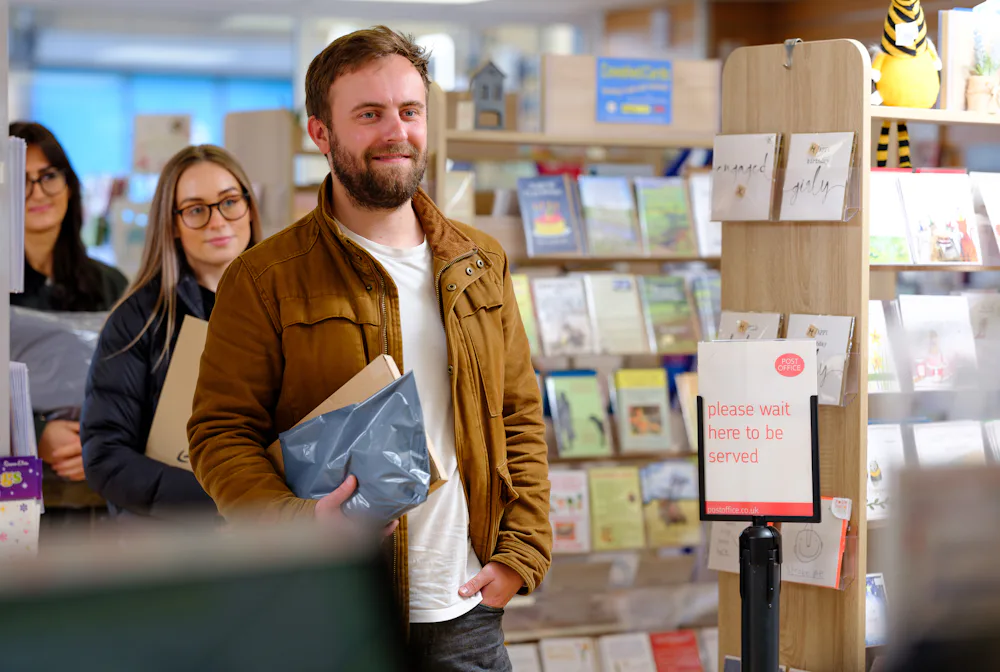 Man with parcel in the queue at a Post Office ParcelShop