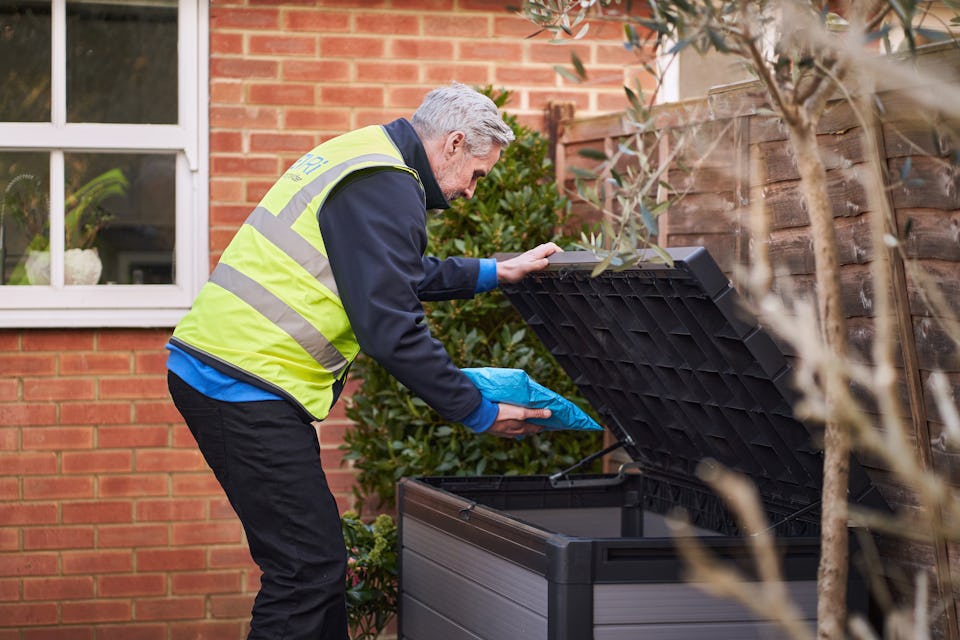 courier outside house opening outdoor storage box to place parcel inside