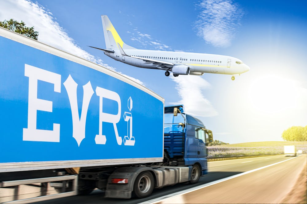 A side profile view shows an Evri branded lorry is driving along a straight road with an aeroplane that can be seen closely above.