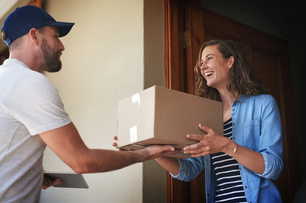 A customer is standing in the doorway of their home, smiling as they are handed a parcel from the courier.