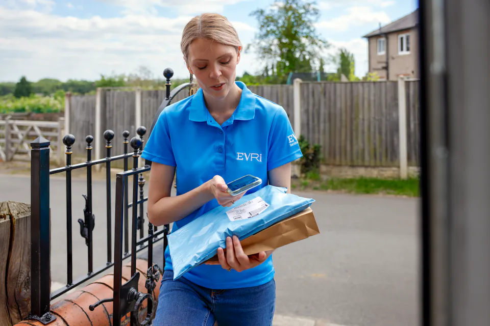 An Evri Courier is scanning the barcode of a parcel at the doorstep of a home in a rural area.