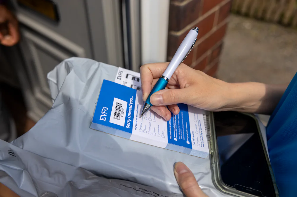 An Evri Courier is taking the name of a neighbour to deliver a missed parcel to. They are filling out a blue slip to post to the intended recipient.