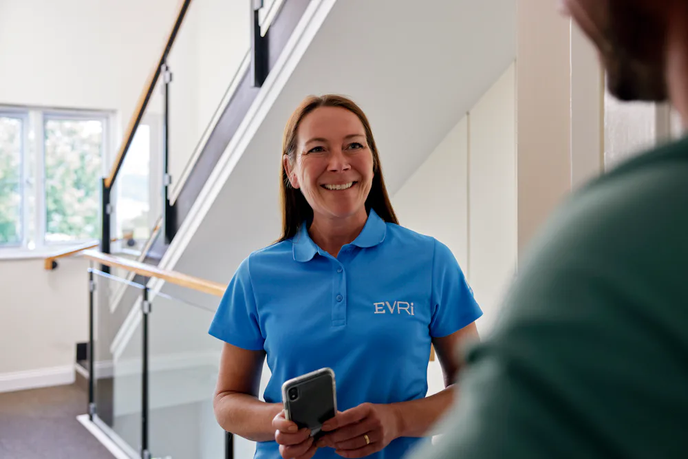 An Evri Courier is conversing with a recipient at their doorstep in a block of flats after a successful parcel delivery.