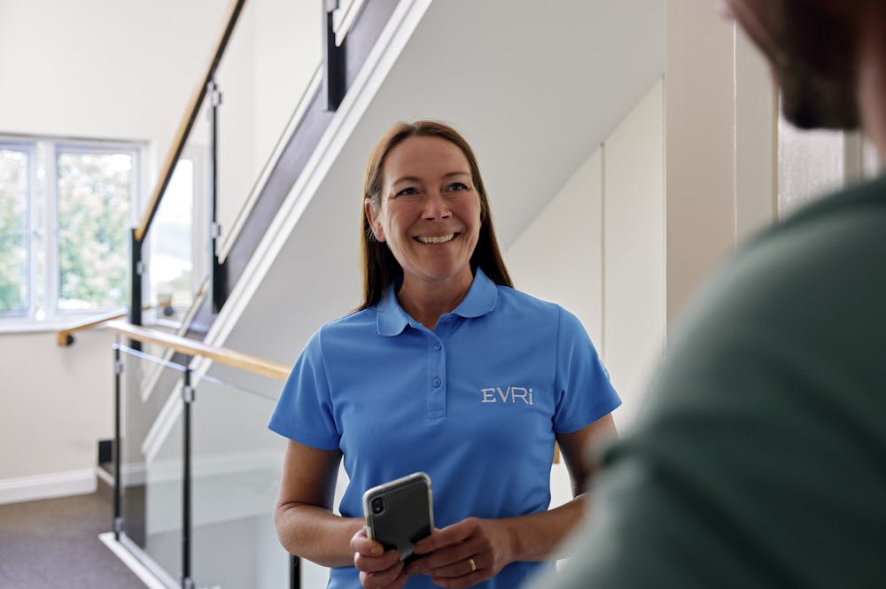 An Evri Courier is conversing with a recipient at their doorstep in a block of flats after a successful parcel delivery.