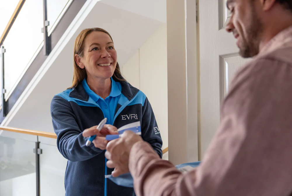 An Evri Courier handing a customer a blue slip to confirm the details of a doorstep parcel collection. The transaction is taking place in a block of flats