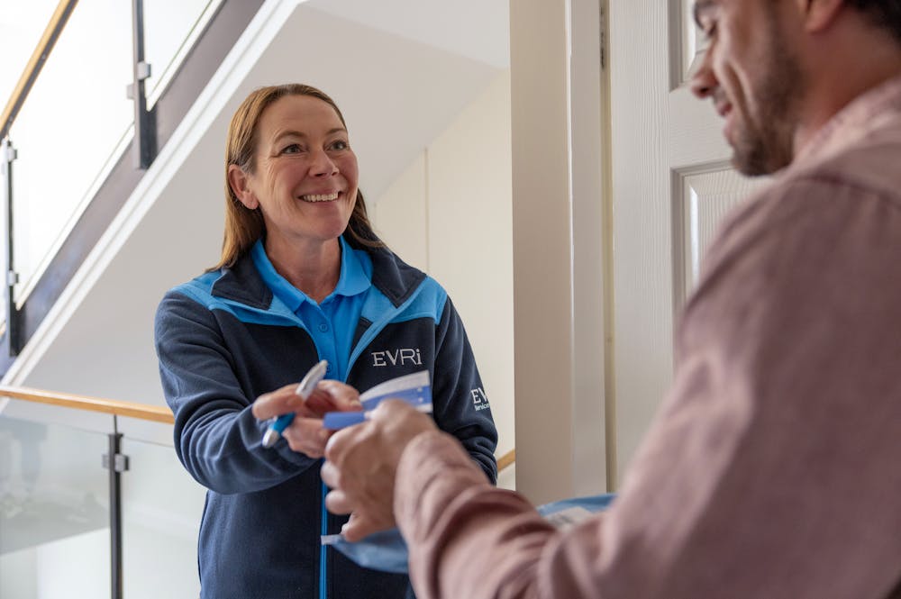 An Evri Courier handing a customer a blue slip to confirm the details of a doorstep parcel collection. The transaction is taking place in a block of flats