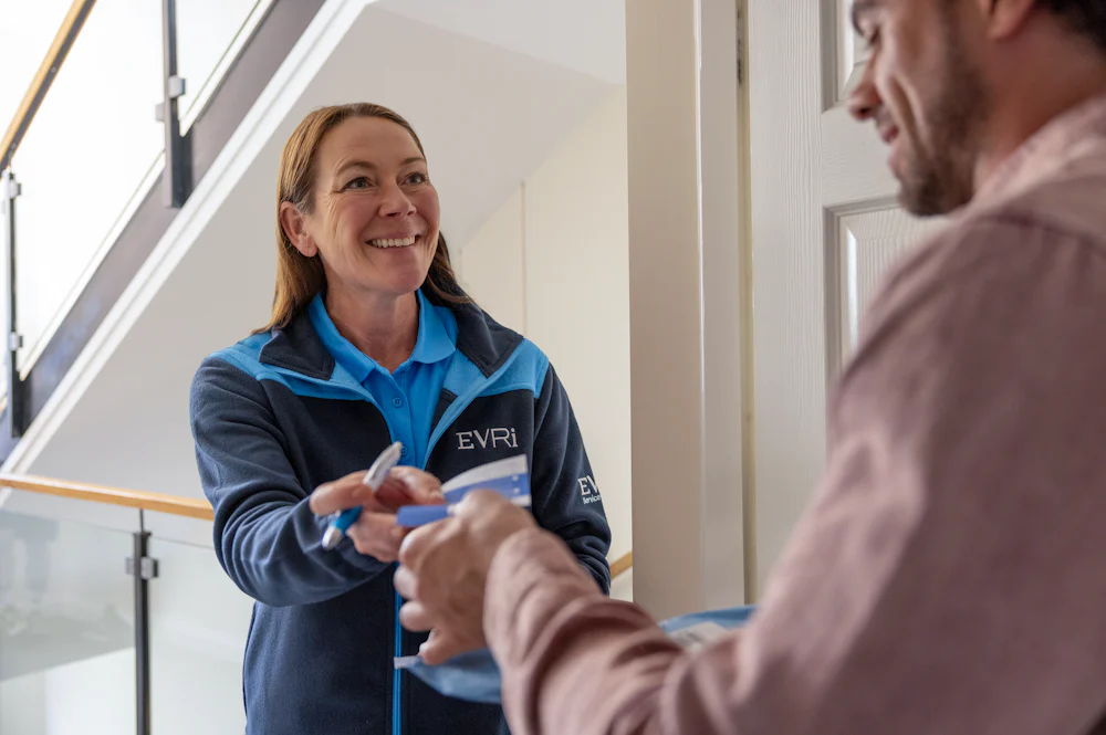 An Evri Courier handing a customer a blue slip to confirm the details of a doorstep parcel collection. The transaction is taking place in a block of flats
