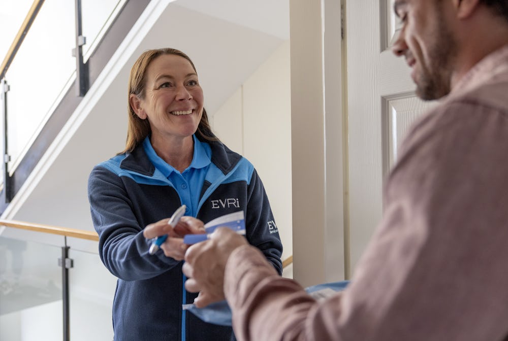 An Evri Courier handing a customer a blue slip to confirm the details of a doorstep parcel collection. The transaction is taking place in a block of flats