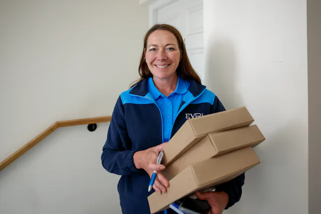 An Evri Courier is smiling posing towards the camera with three parcels in their grasp.