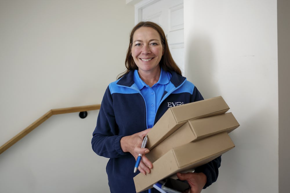 An Evri Courier is smiling posing towards the camera with three parcels in their grasp.