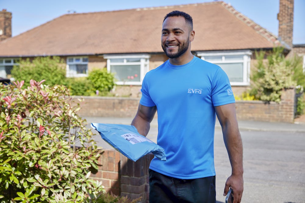 An Evri Courier is approaching the doorstep of a house in a residential area. He is carrying a single parcel, ready to deliver it.