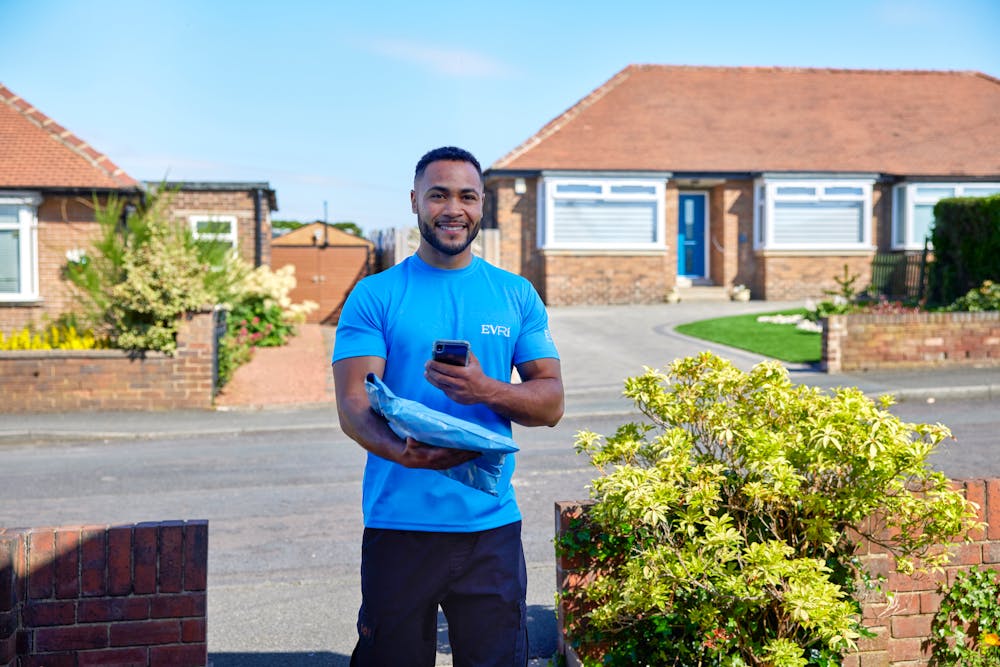 An Evri Courier is scanning the barcode of a single parcel as he approaches the doorstep of a home in a residential area. He is there to make a delivery.