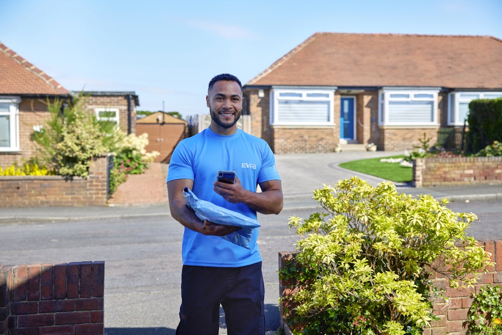 An Evri Courier is scanning the barcode of a single parcel as he approaches the doorstep of a home in a residential area. He is there to make a delivery.