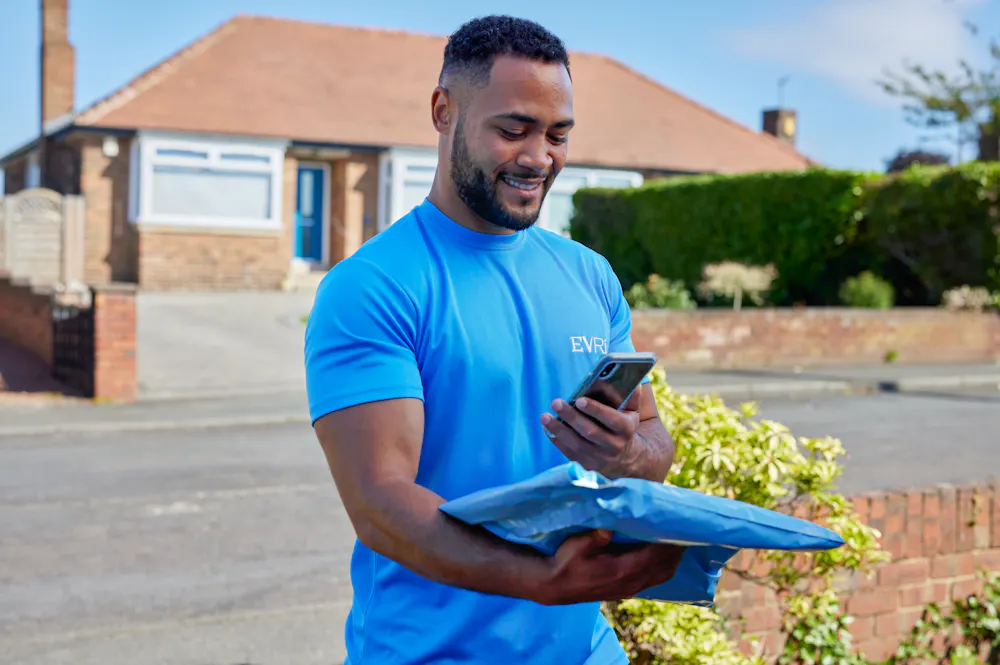 An Evri Courier is scanning the barcode of a single parcel as he approaches the doorstep of a home in a residential area. He is there to make a delivery.