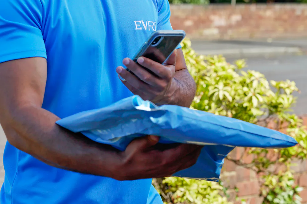 An Evri Courier is scanning the barcode of a single parcel as he approaches the doorstep of a home in a residential area. He is there to make a delivery.