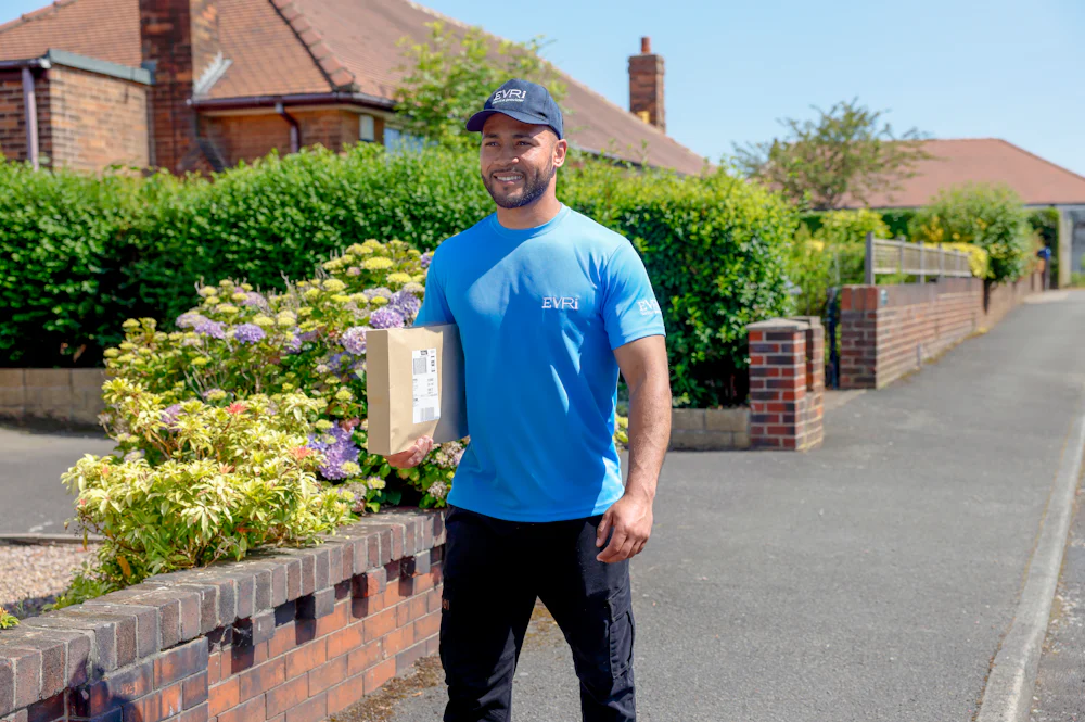 An Evri Courier is walking down the street in a residential area with a parcel under his arm.