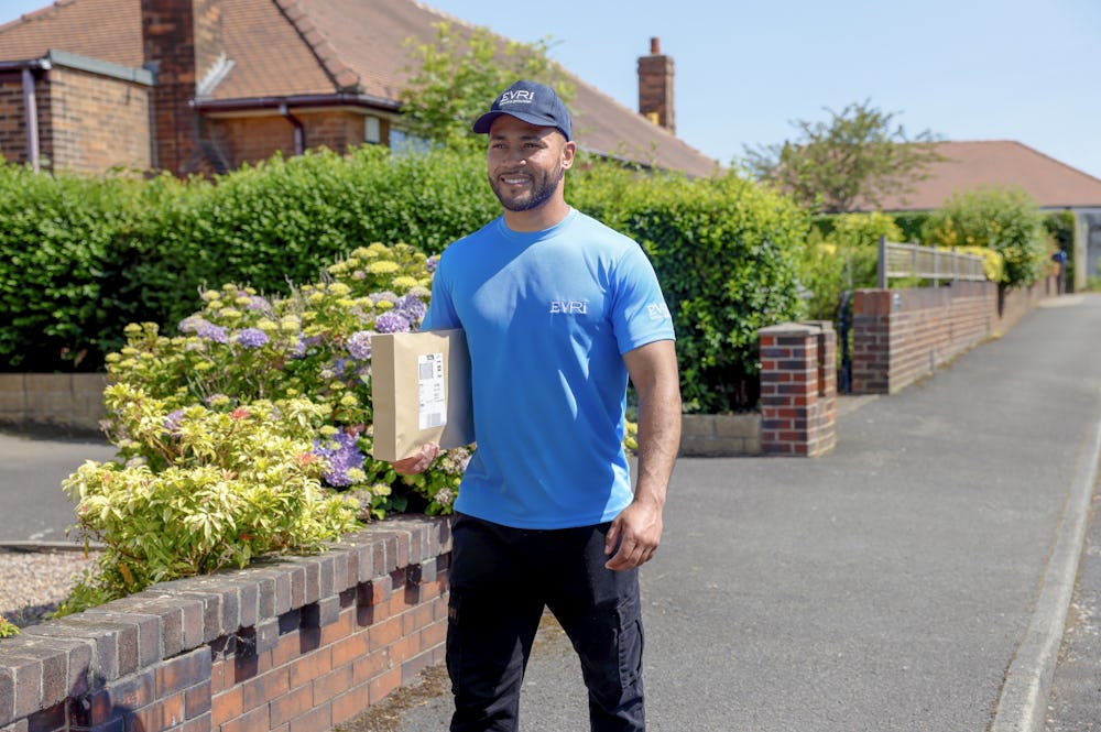 An Evri Courier is walking down the street in a residential area with a parcel under his arm.