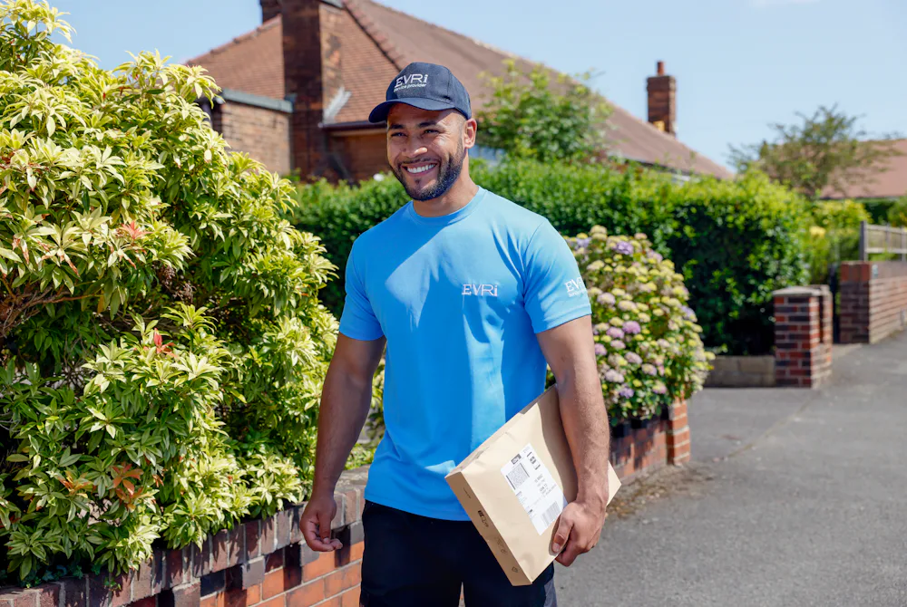 An Evri Courier is walking down the street in a residential area with a parcel under his arm.