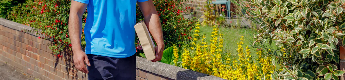 An Evri Courier is walking down the street in a residential area with a parcel under his arm.