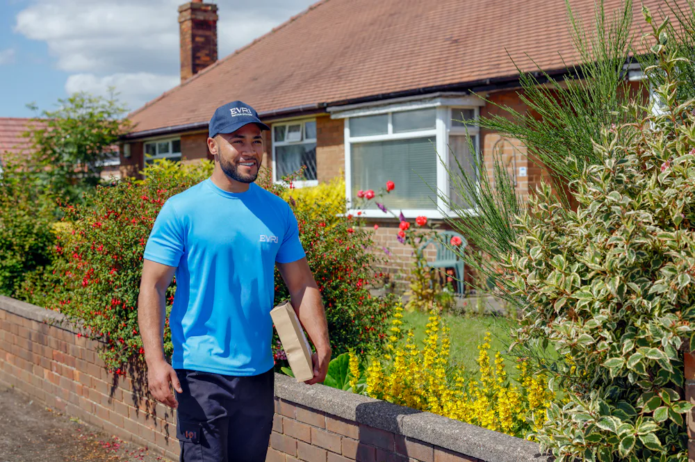 An Evri Courier is walking down the street in a residential area with a parcel under his arm.