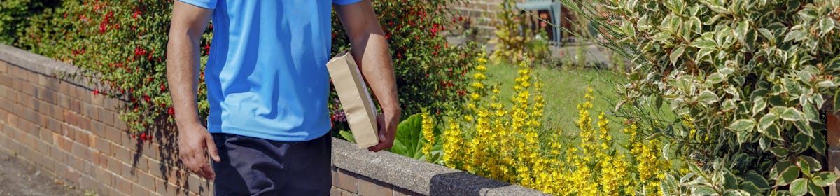 An Evri Courier is walking down the street in a residential area with a parcel under his arm.