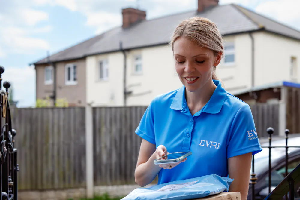 An Evri Courier is scanning the barcode of a parcel at the doorstep of a home in a rural area.