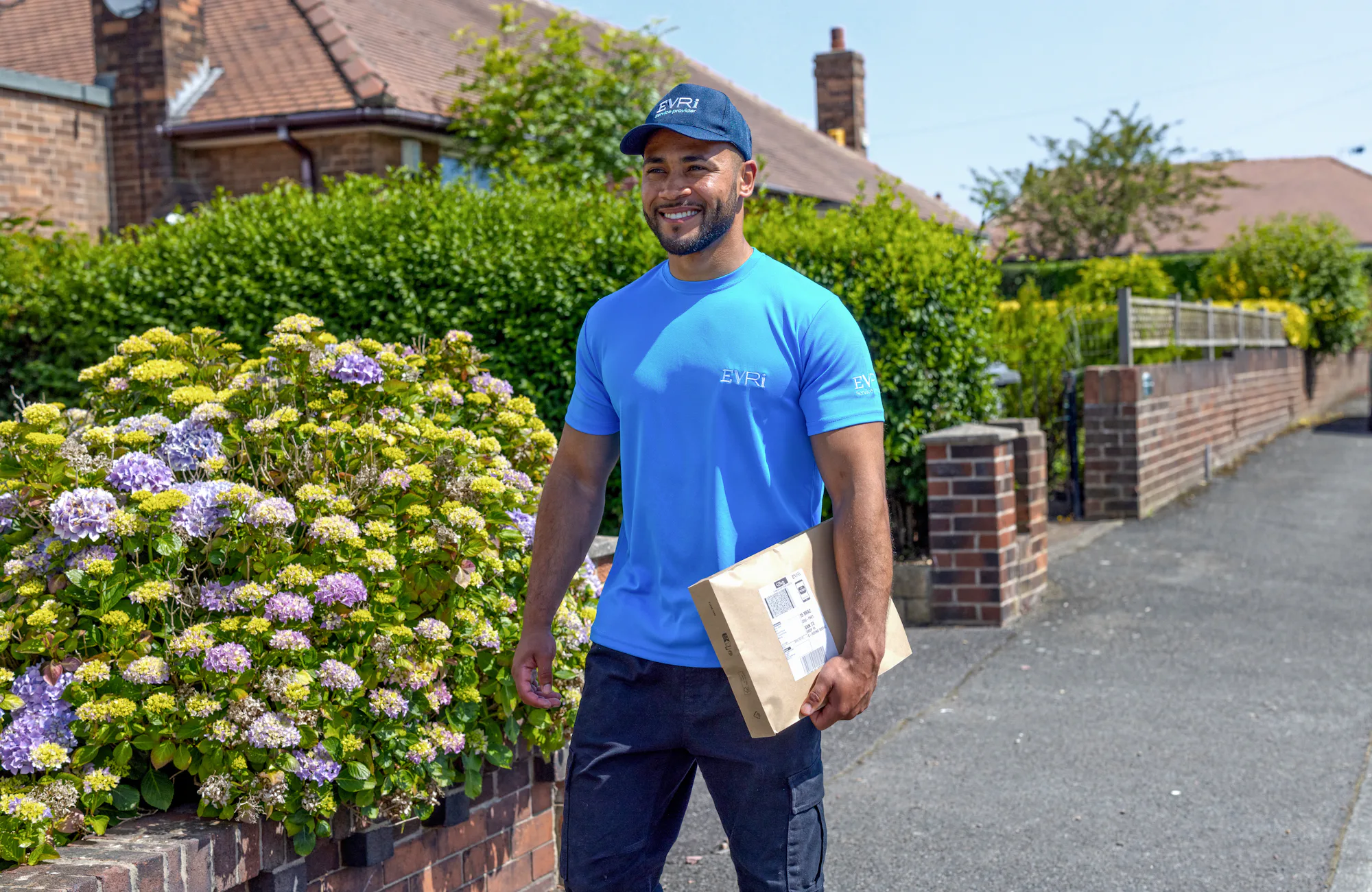 An Evri Courier is walking down the street in a residential area with a parcel under his arm.