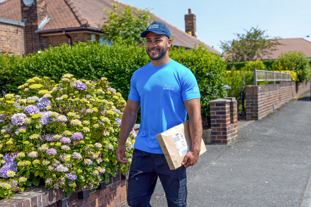 An Evri Courier is walking down the street in a residential area with a parcel under his arm.
