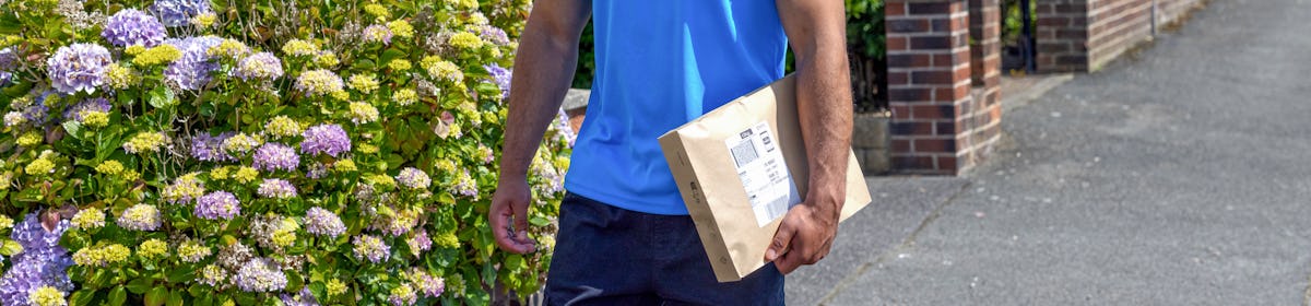 An Evri Courier is walking down the street in a residential area with a parcel under his arm.