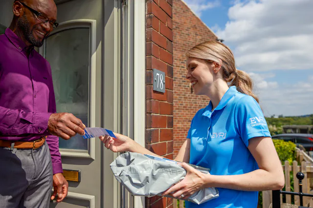 A customer has just handed their parcel to an Evri courier as a part of a doorstep collection. The customer is being handed a blue slip as a receipt of the transaction.