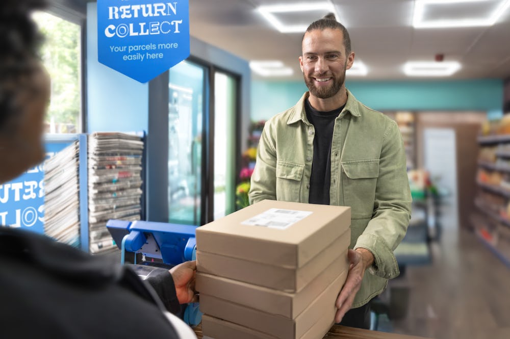 Customer inside a ParcelShop store, handing multiple parcels to store assistant, ready to be collected by Evri