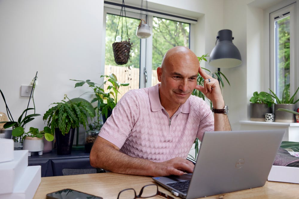 Customer sat at a desk in their office using a laptop with multiple parcels packaged next to them. Their hand is positioned against their head to show concentration.