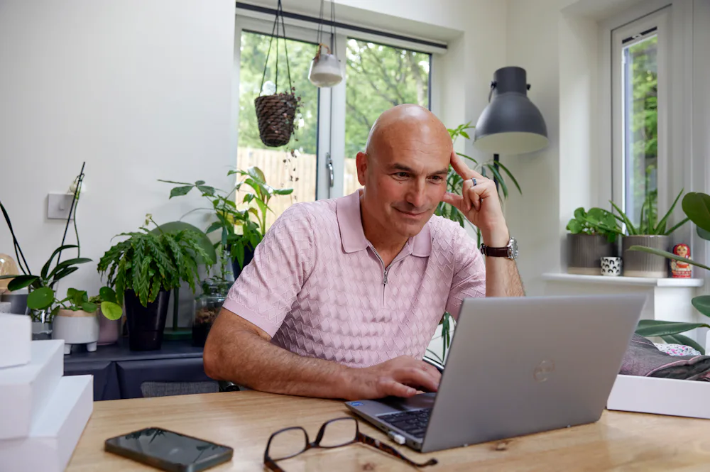 Customer sat at a desk in their office using a laptop with multiple parcels packaged next to them. Their hand is positioned against their head to show concentration.