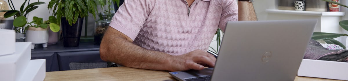 Customer sat at a desk in their office using a laptop with multiple parcels packaged next to them. Their hand is positioned against their head to show concentration.