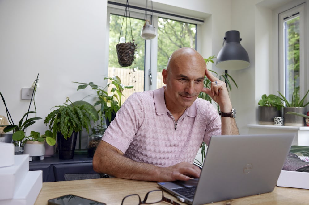 Customer sat at a desk in their office using a laptop with multiple parcels packaged next to them. Their hand is positioned against their head to show concentration.