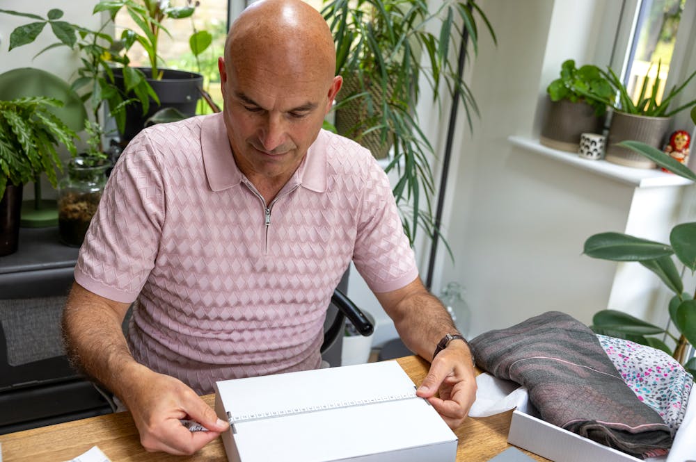 Customer sat at a desk holding a tape measure across their parcel to measure its size.